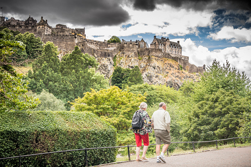 Edinburgh, Scotland - July 14, 2022:  A senior couple walk in the Princes Street Gardens bellow the Edinburgh castle.