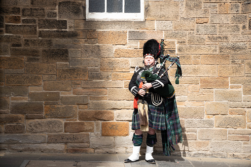 Scottish bagpiper in the Highlands of Scotland, panoramic mountains landscape background, UK