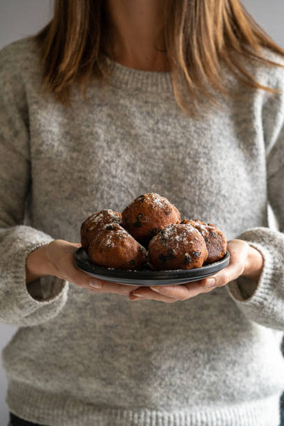 a woman holding a plate of oliebollen (dutch doughnuts) dusted with icing sugar - oliebollen stockfoto's en -beelden