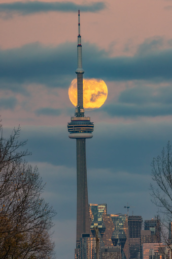 Toronto, Ontario - November 7, 2022 : A full moon rises through clouds behind the CN Tower at dusk