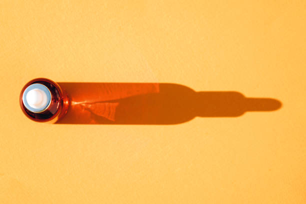 istock View above glass dropper bottle with face serum over orange background with bottle shape shadow. Beauty skin-care products, natural face beauty oil with vitamin C 1453831282