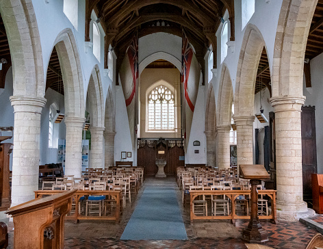 A view from the chancel along the nave towards the baptismal font and vestry in All Saints parish church in Burnham Thorpe, Norfolk, Eastern England. The church was originally built in the 13th century but was renovated in the 1840s and further restored in 1905 in commemoration of the centenary of Lord Nelson’s victory at the Battle of Trafalgar. The Admiralty presented timbers from Nelson’s ship, HMS Victory, to build the altar, lectern and rood screen. Horatio, later Lord, Nelson was born and baptised in the village of Burnham Thorpe, where his father Edmund Nelson was the rector. Two White Ensigns hang from the ceiling - the church has the unique right to fly the White Ensign from its tower and does so each Trafalgar Day, 21st October. The church is a favourite with admirers of Lord Nelson.