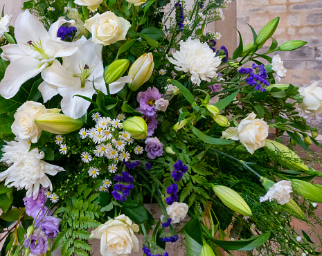 A display of purple, mauve and white flowers in a church. The flowers include lilies, roses, daisies, ferns, gypsophila, chrysanthemums and many others.
