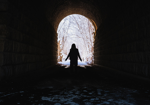 View of silhouette of woman standing in dark former railroad tunnel  in winter; snow covered trees in background
