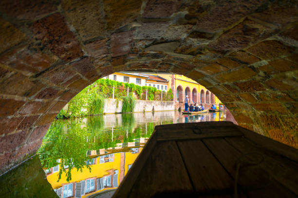 A boat glides through a canal surrounded by medieval half timber buildings in the Petite Venice district of Colmar, France.