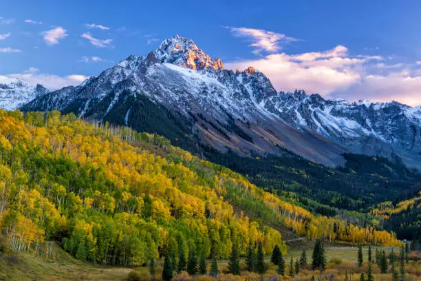 The last light of the setting sun hits the crags atop Mount Sneffels, with a mostly golden grove of quaking aspens below, in the San Juan Mountains near Ridgway, Colorado.