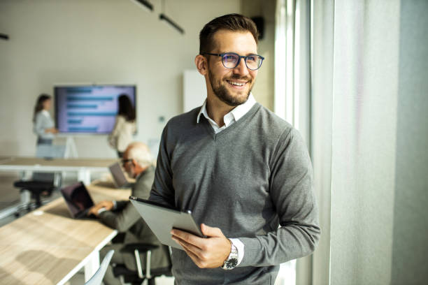 retrato de un joven empresario usando una tableta después de una reunión en la oficina - mid adult men smart casual white happiness fotografías e imágenes de stock