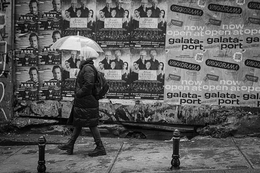 Istanbul, Turkey – February 03, 2022: A grayscale shot of a woman passing by a street in Istanbul next to a wall has advertise posters in Istanbul