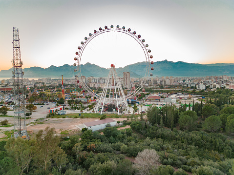 City view taken by drone plane at hour close to sunset. We see the sea, ferris wheel, amusement park, mountains and nature.