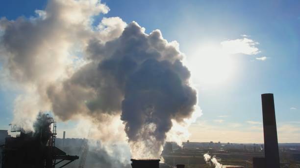 vista de tubos altos da usina siderúrgica e de mineração com chaminé branca. vista aérea de cachimbos de chaminé alta com fumaça cinza da instalação de fabricação. fumaça se movendo e bloqueando o pôr do sol, vazamentos de luz piscando - rasto de fumo de avião - fotografias e filmes do acervo