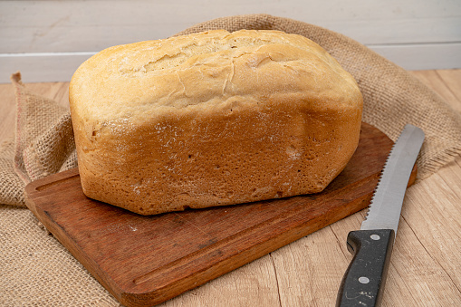 A Homemade bread last made with a bread machine on a wooden board with a bread knife. Space for text.