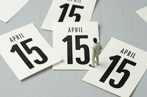 Businessman figurine looking at calendar leaves. Tax Day concept.