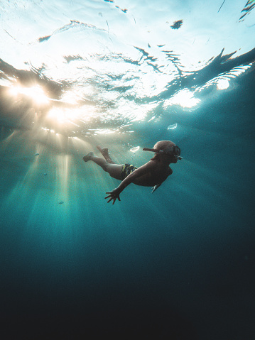 Beautiful underwater shot of a Caucasian young boy diving in turquoise colored sea. He is exploring and looking for adventures. He is wearing swimwear.