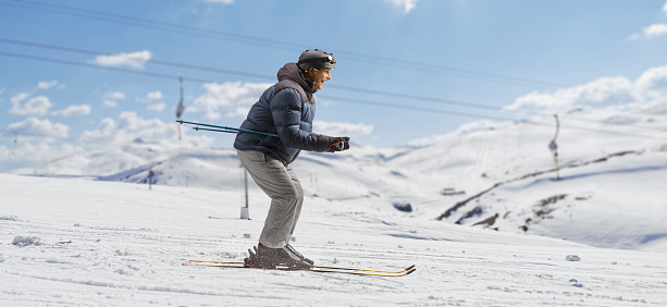 Full length profile shot of a mature man skiing downhill on a mountain