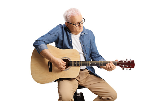 Mature musician sitting on a chair and playing an acoustic guitar isolated on white background