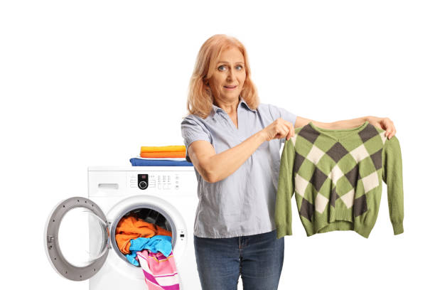 mature woman taking a green sweather out of a washing machine - shrank imagens e fotografias de stock