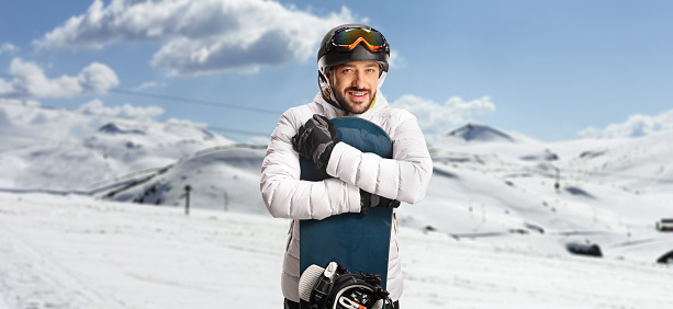Young man hugging a snowboard and posing on a snowy mountain