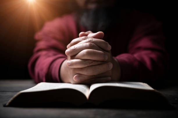 Hands folded in prayer on a Holy Bible in church concept for faith, spirituality and religion, man praying in morning. Man hand with Bible praying. Person Christian who faith in Jesus worship in dark. manos cruzadas en oración sobre una santa biblia en concepto de iglesia para la fe, la espiritualidad y la religión, el hombre orando en la mañana. mano del hombre con la biblia orando. persona cristiana que fe en jesús adorar en la oscuridad.