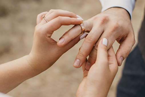 At the wedding ceremony, the bride puts the wedding ring on the groom's finger. Hands of newlyweds with wedding rings close-up. Heterosexual young couple in love at the moment of the wedding ceremony