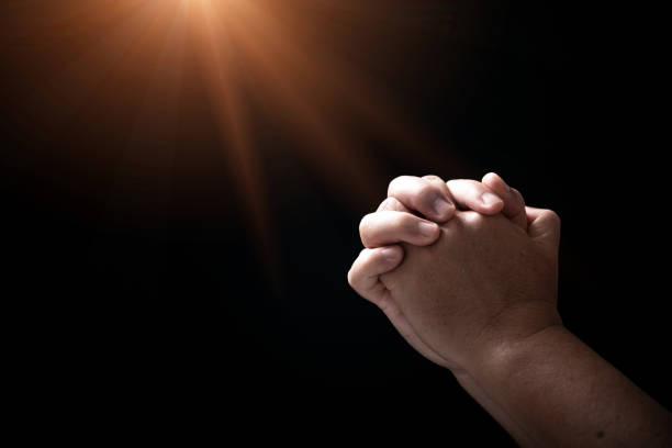 Hands folded in prayer on in church concept for faith, spirituality and religion, man praying in the morning. man hand with praying god. Person Christian men who have faith in Jesus worship in dark. stock photo