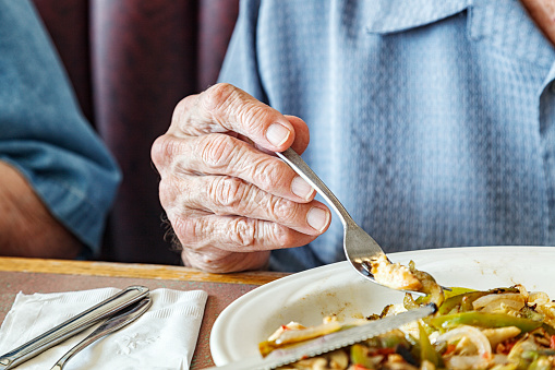 Real life, real person elderly senior adult man's hand holding his breakfast fork as he eats his meal in a diner café restaurant. He is sitting next to his off-camera senior adult woman wife. He's having his favorite breakfast plate - scrambled eggs with vegetables including onions and peppers.