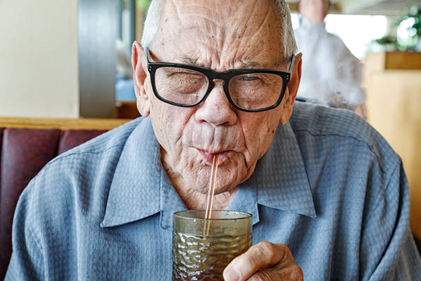 istock Thirsty Senior Man Squinting Sucking Water Through Straw at Restaurant 1453879988