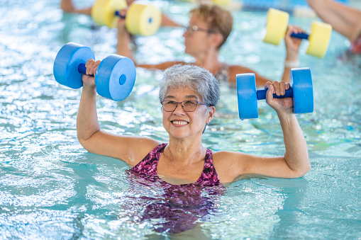 A group of happy seniors taking a water aerobics class at a community centre. The women use various pool equipment to exercise.