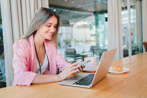 Attractive young business woman using computer, with mug of coffee in modern workplace. Millennial generation. Role of women in the business world.