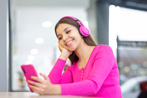 Young woman smiling while listening to music and watching her cell phone