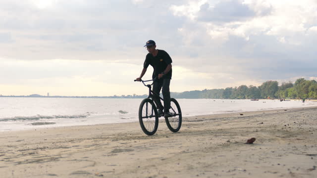 Cyclist man riding fixed gear extreme sport bike in sunny day on tropical beach. Healthy lifestyle and exercise.