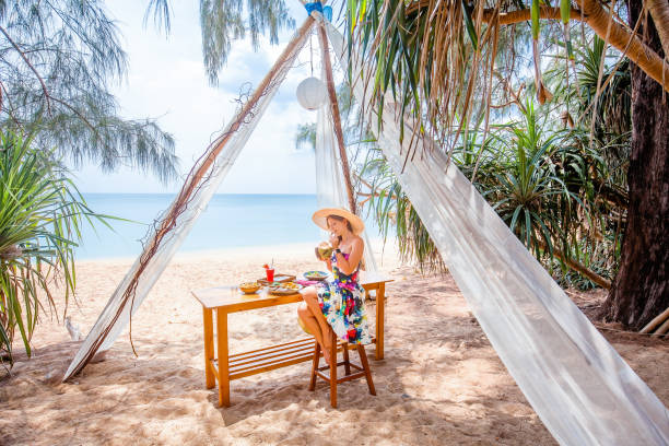 istock Woman sitting at beach table, enjoy sea view, drinking fresh coconut 1453901028