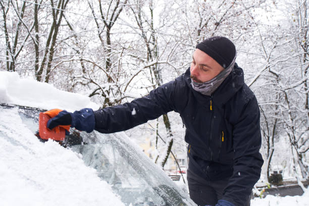 istock Man cleans his car after a snowfall. Cleaning snow from windshield, Scraping ice, Winter car window cleaning 1453901146