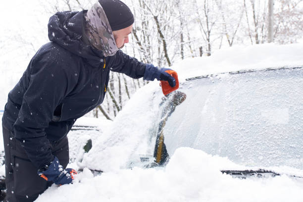 istock Man cleans his car after a snowfall. Cleaning snow from windshield, Scraping ice, Winter car window cleaning 1453901157