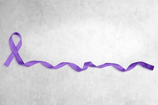 Photo of purple ribbon with curled end atop a light concrete background with copy space.