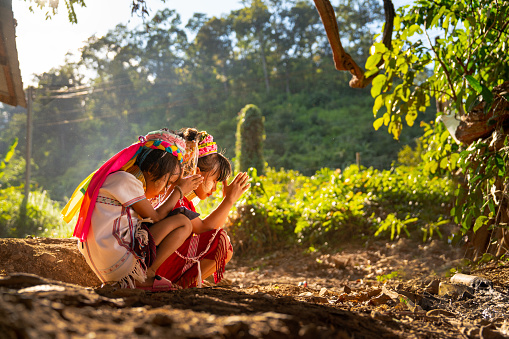 Two little Asian hill tribe children sit and pray to the right side to worship spirit or angel in the Karen Long Neck village.