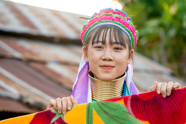 Lovely AsianLong Neck Karen girl hold multicolor blanket on clothesline and look at camera with smiling and house roof as background. Lovely AsianLong Neck Karen girl hold multicolor blanket on clothesline and look at camera with smiling and house roof as background. padaung tribe stock pictures, royalty-free photos & images