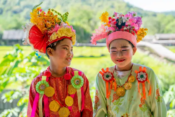 Photo of Asian boy with Poy Sang Long cloths style stand with relax position during wait to joy the festival and they smile with happiness with garden and grass field as background.