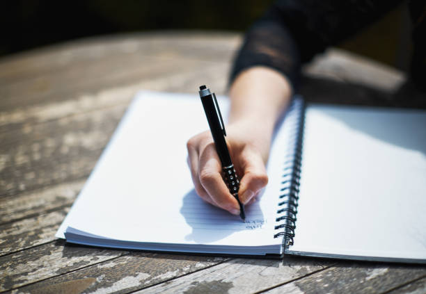 Young woman writing in spiral notebook at outdoor table stock photo