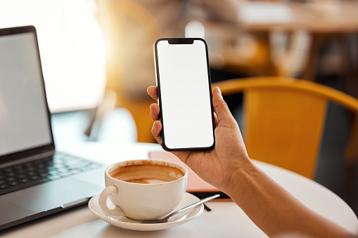 Closeup of a female hand holding phone with copy space while sitting in a modern coffee shop. Woman working on technology browsing on the internet, social media or an online website at a cafeteria.