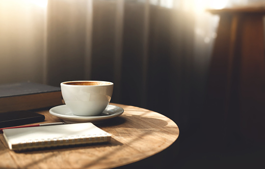 Close up view, white coffee cup with old book and smart phone on wooden table near the window and the sun is shining through, vintage color tone