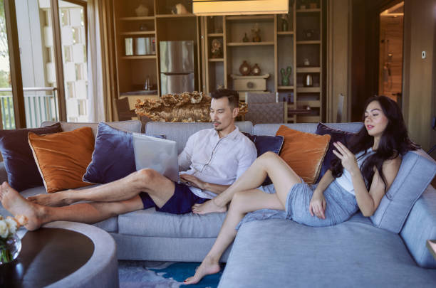 istock Young asian couple relaxing or working online sitting on a couch at home, using laptop computer and mobile phone. Modern technology and lifestyle concept 1453915476