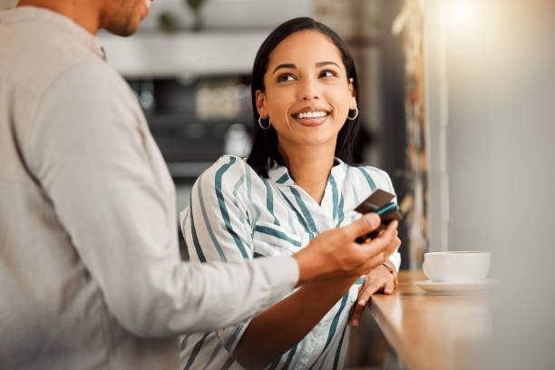 Female customer paying using contactless credit card, standing by cafe or restaurant bar counter. Smiling woman make cashless payment for coffee bill with wireless NFC tag reader technology machine. cliente que paga con tarjeta de crédito sin contacto, de pie junto a la barra del bar de la cafetería o del restaurante. mujer sonriente hace el pago sin efectivo de la factura del café con la tecnología inalámbrica de lector de etiquetas nfc pos máq