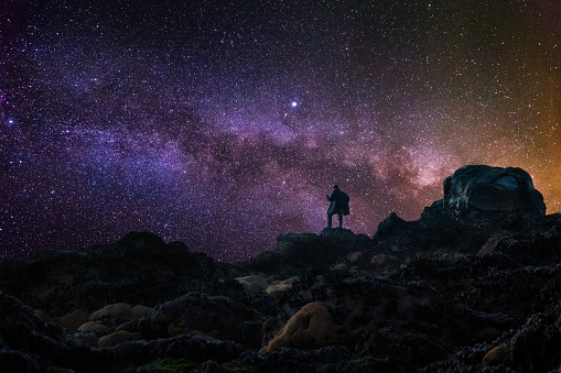 Silhouette of a man standing on a rocky mountain at night and looking at Milky Way. Inspiring view of stars in the sky.