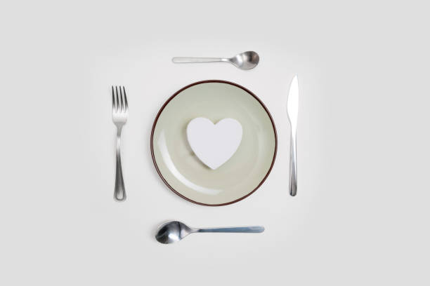 Romantic valentines day dinner idea concept. Heart on plate and silver wear on white background.