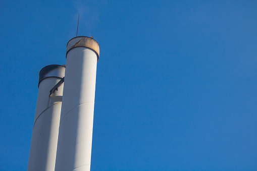 A low angle shot of chimneys of a wood pellet power plant for local heating supply against a blue sky