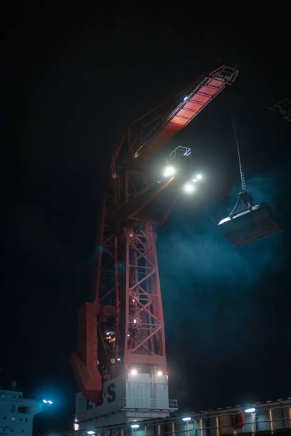 Rotterdam, Netherlands – September 17, 2020: A big crane in the harbor of Rotterdam unloading a bulk carrier and loading a riverboat at night
