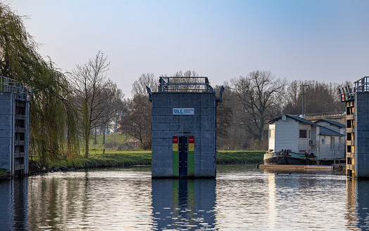 Roermond, Netherlands – March 31, 2022: A floodgate in Roermond, Netherlands holding back the river Maas. With a houseboat behind it