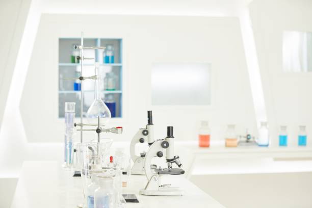 istock Side view of two microscopes next to beakers filled with fluid and other laboratory equipments. 1453933976