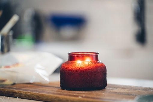 A candle in a red glass container on the wooden board