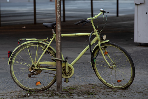 A green bicycle tied to a metal pole in the street